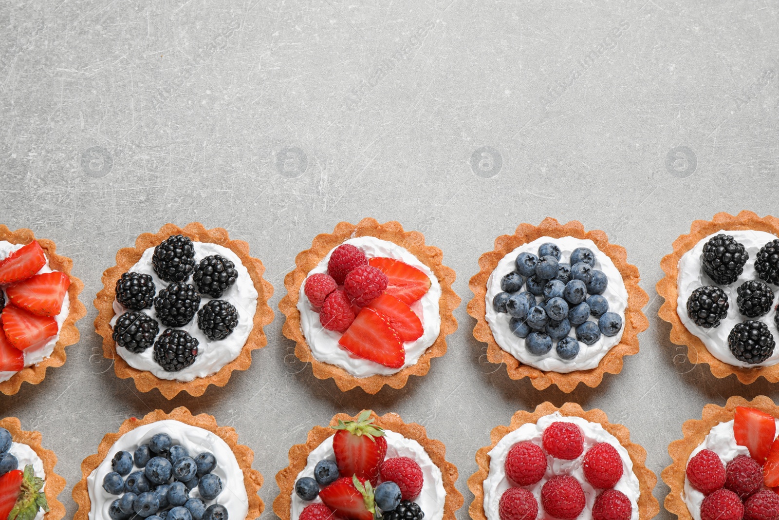 Photo of Many different berry tarts on table, flat lay with space for text. Delicious pastries