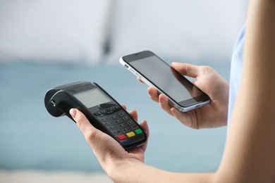 Woman using modern payment terminal with mobile phone indoors, closeup