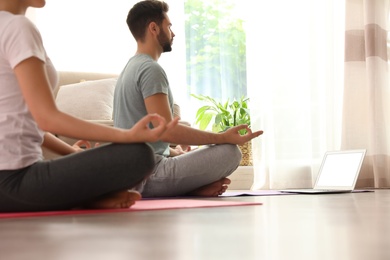 Photo of Couple practicing yoga while watching online class at home during coronavirus pandemic. Social distancing