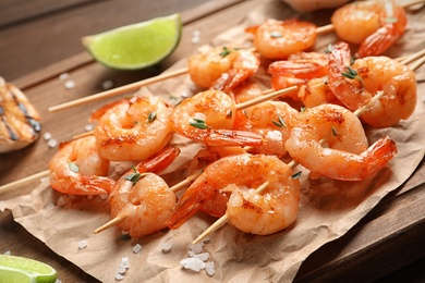 Photo of Skewers with delicious fried shrimps on wooden board, closeup