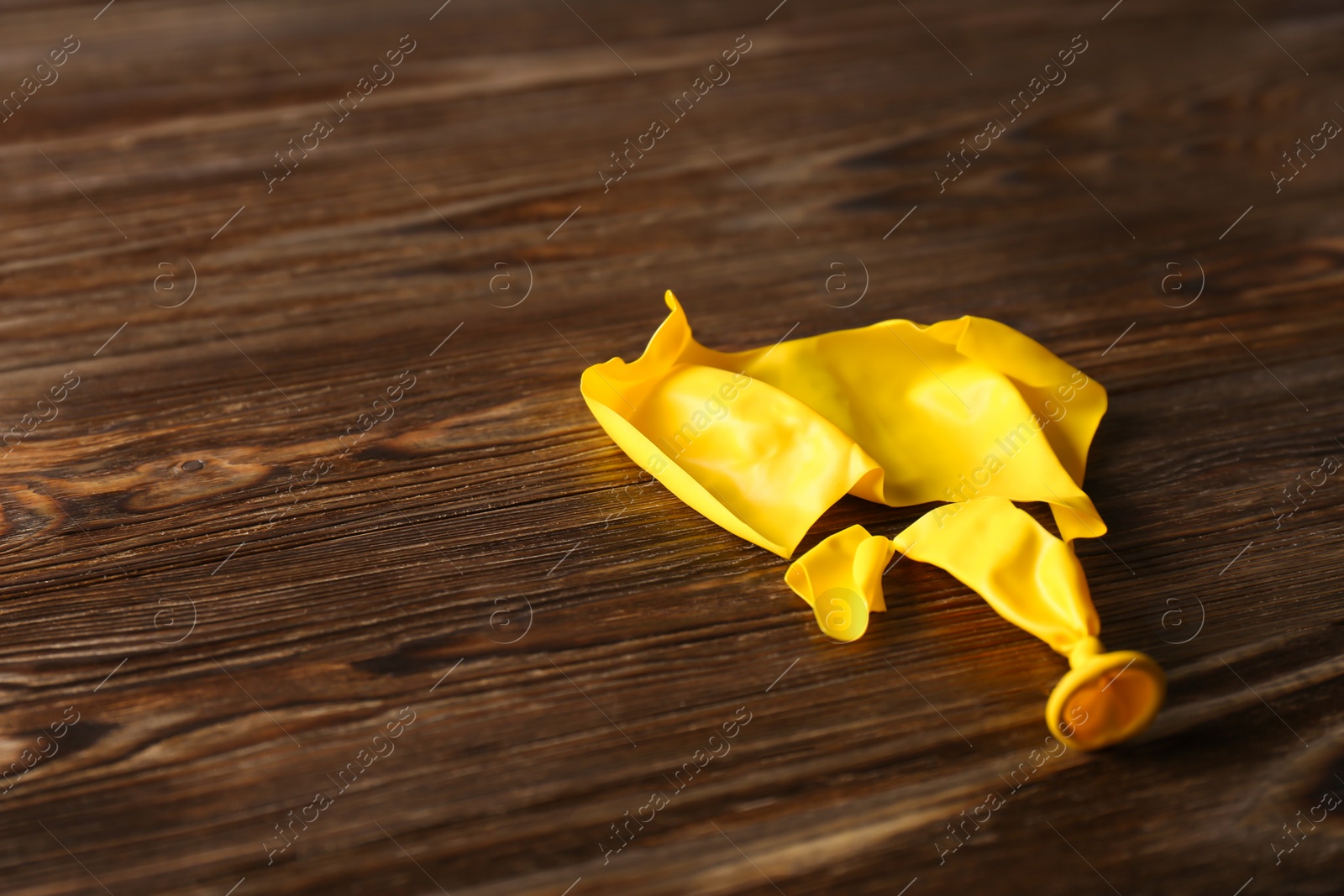 Photo of Popped yellow balloon on wooden background, space for text