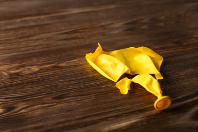 Photo of Popped yellow balloon on wooden background, space for text