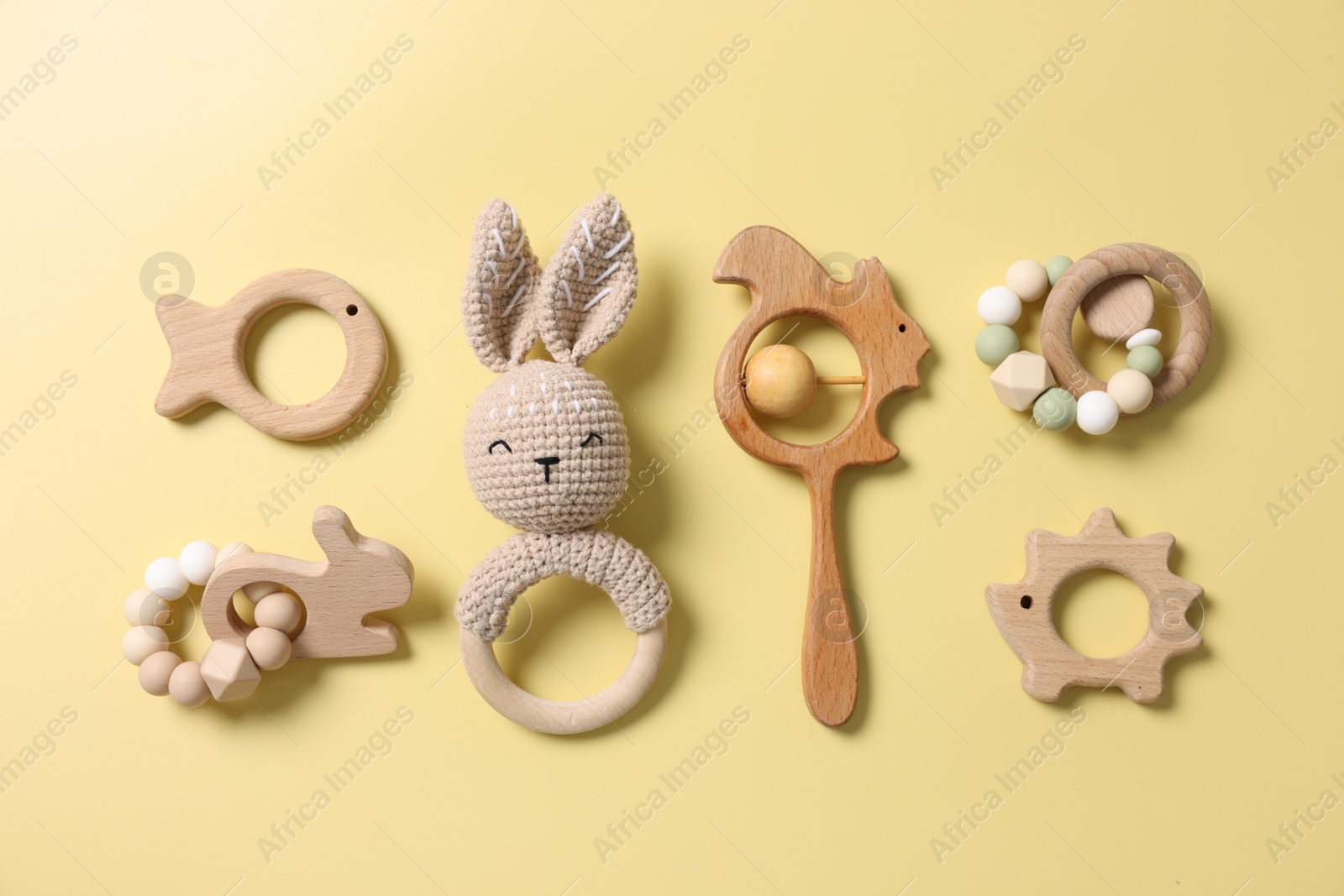Photo of Baby accessories. Rattles and teethers on yellow background, flat lay