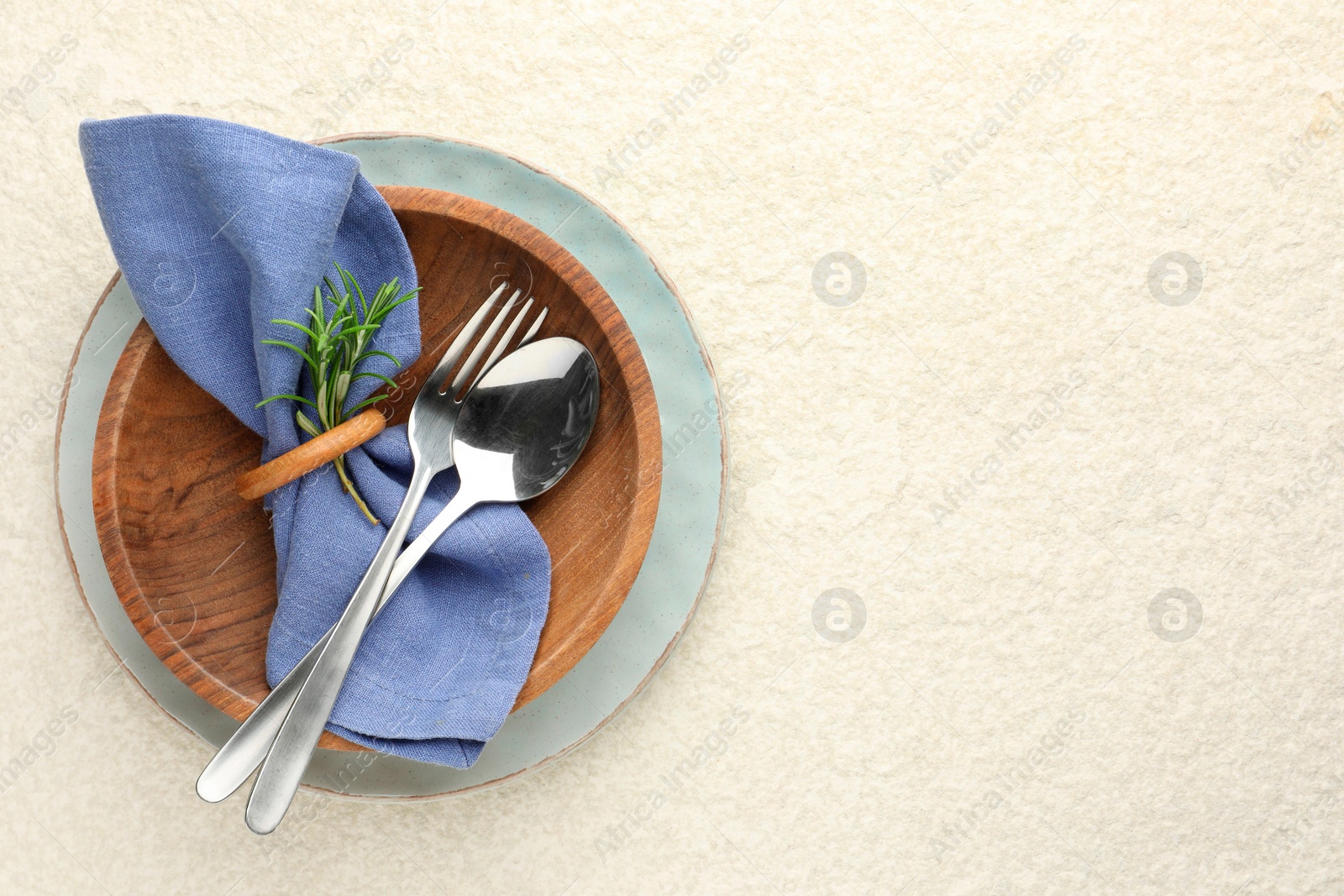 Photo of Stylish setting with cutlery, napkin, rosemary and plates on light textured table, top view. Space for text