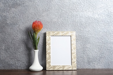 Photo of Blank frame and vase with flower on table near color wall. Mock up for design