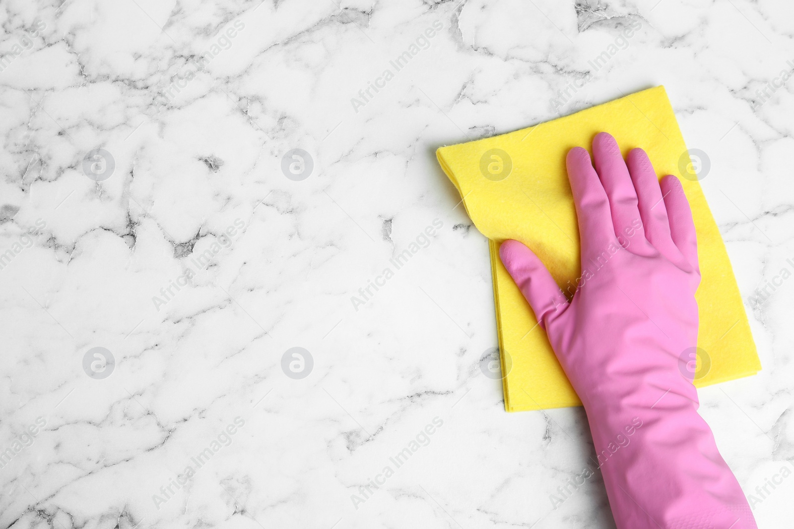 Photo of Woman in gloves wiping white marble table with rag, top view. Space for text