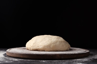Photo of Wooden board with flour and bread dough on table against dark background. Space for text
