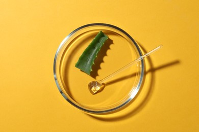 Petri dish with aloe vera and glass stirring rod on yellow background, top view
