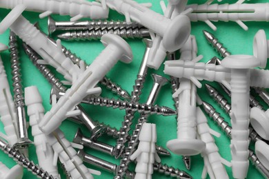 Photo of Many metal screws and white dowels on turquoise background, closeup