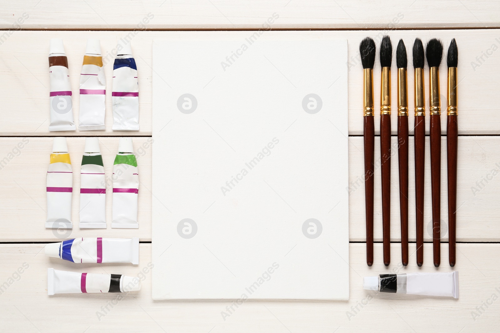 Photo of Blank canvas, brushes and paints on white wooden table, flat lay. Space for text