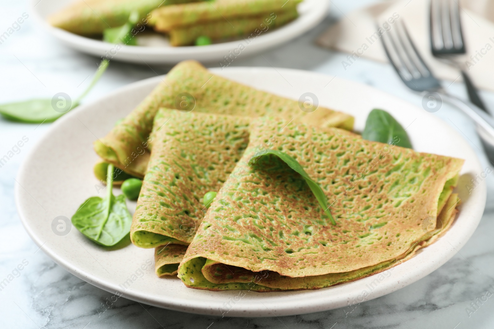 Photo of Tasty spinach crepes on white marble table, closeup