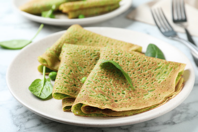 Tasty spinach crepes on white marble table, closeup