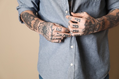 Photo of Young man with tattoos on body against beige background, closeup