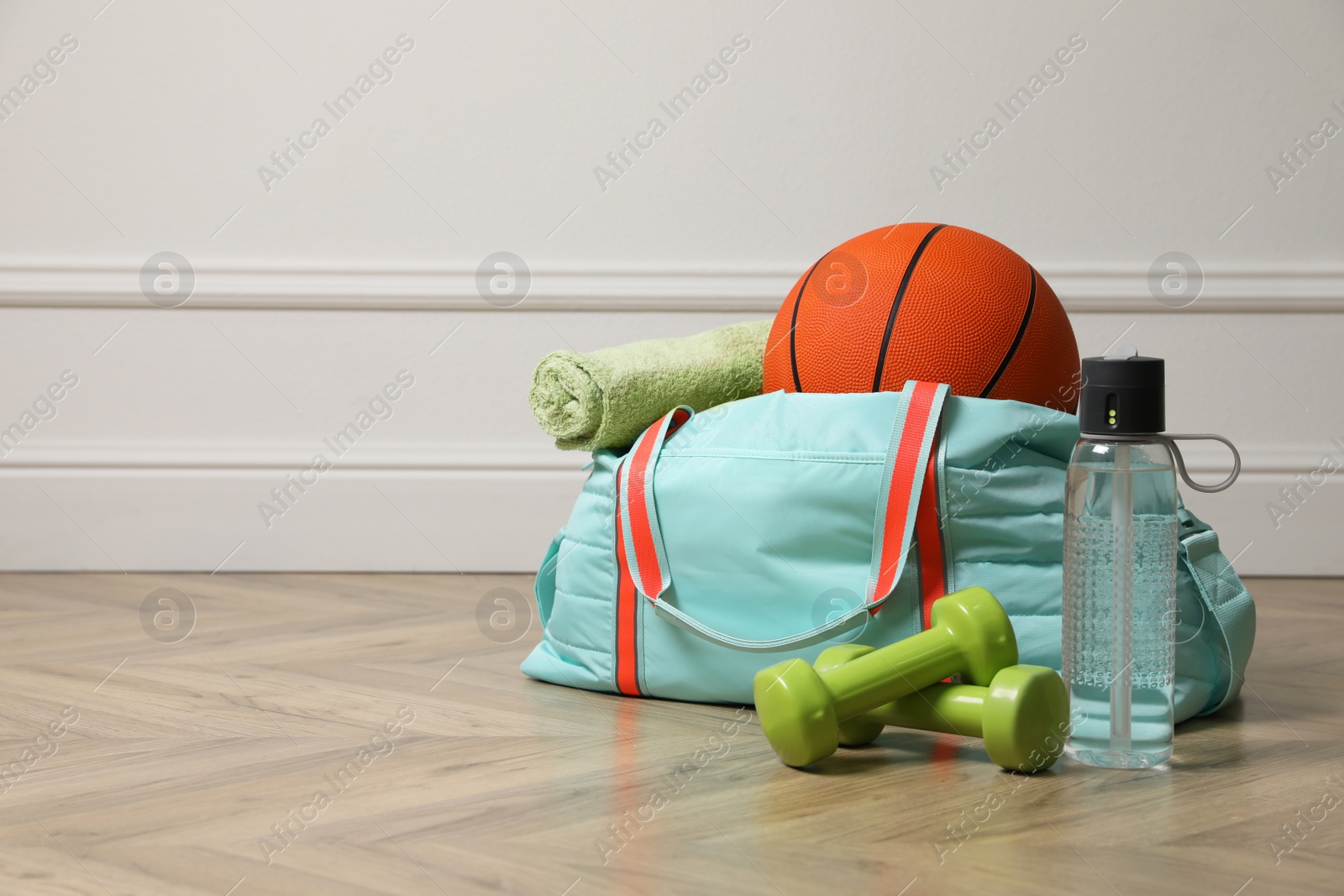 Photo of Blue gym bag with sports accessories on floor near white wall indoors, space for text