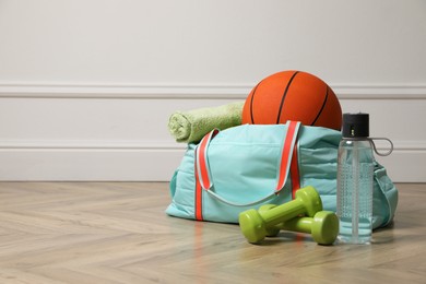 Photo of Blue gym bag with sports accessories on floor near white wall indoors, space for text