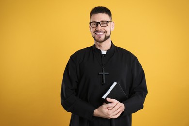 Priest in cassock with Bible on yellow background