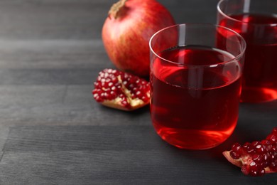 Photo of Tasty pomegranate juice in glasses and fresh fruits on black wooden table, closeup. Space for text