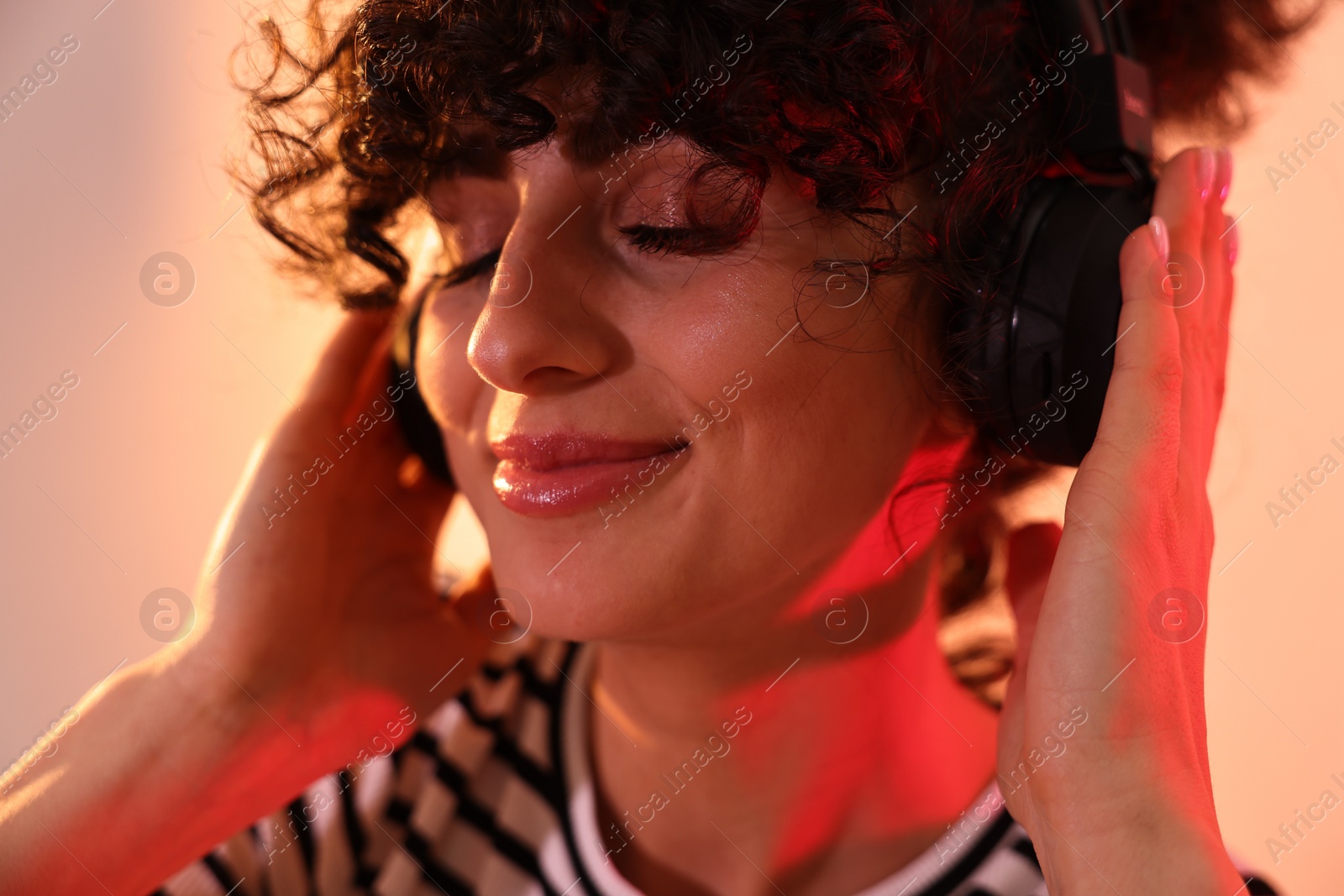 Photo of Beautiful young woman listening to music with headphones on color background in neon lights, closeup