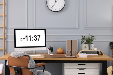 Stylish workplace with computer, houseplant and stationery on wooden desk near grey wall at home