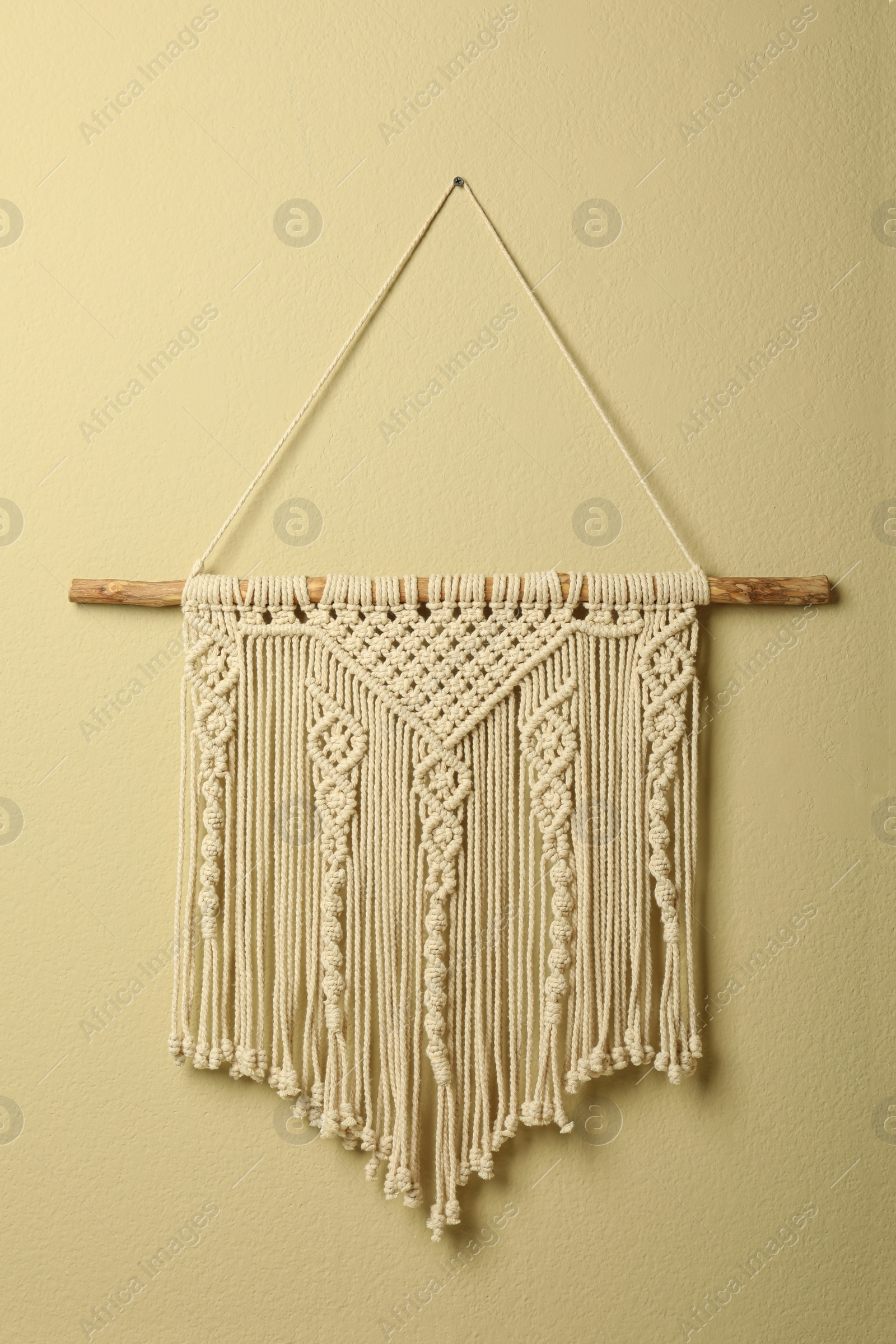 Photo of Beautiful macrame hanging on beige wall. Decorative element