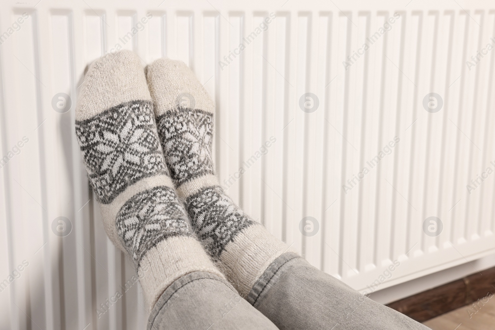 Photo of Woman warming feet near heating radiator, closeup