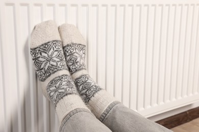 Photo of Woman warming feet near heating radiator, closeup
