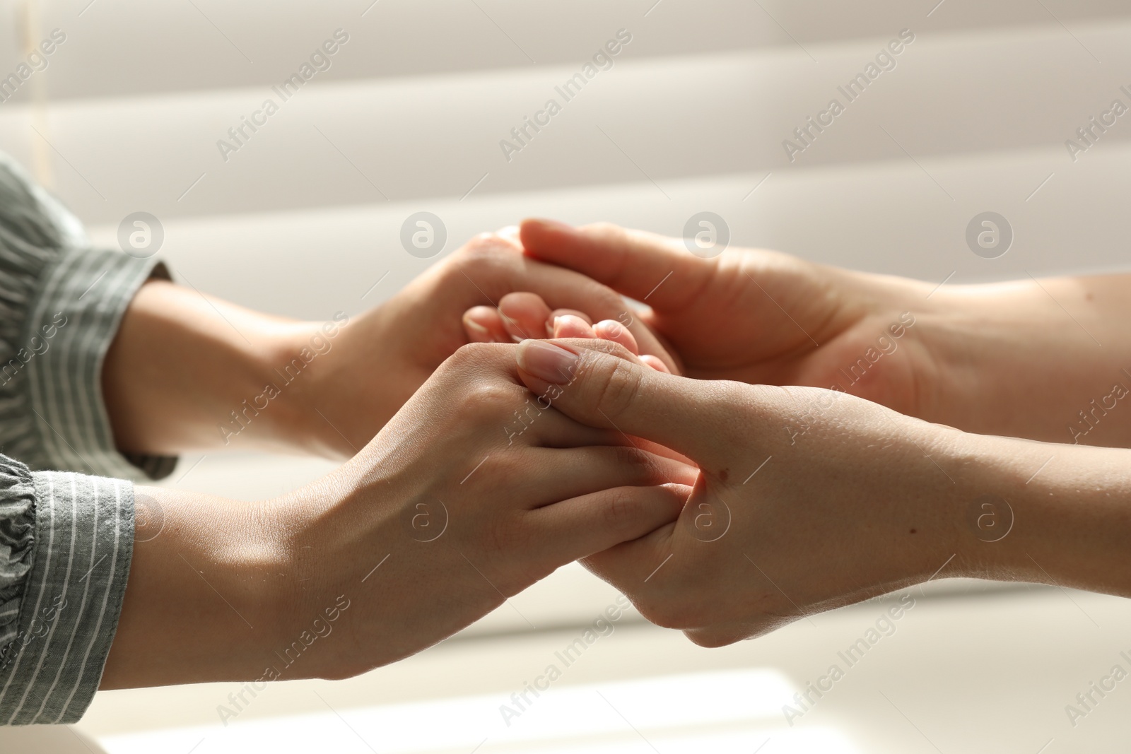 Photo of Religious women holding hands and praying together near window indoors, closeup