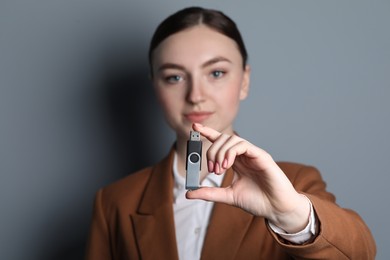 Photo of Woman holding usb flash drive on grey background, closeup