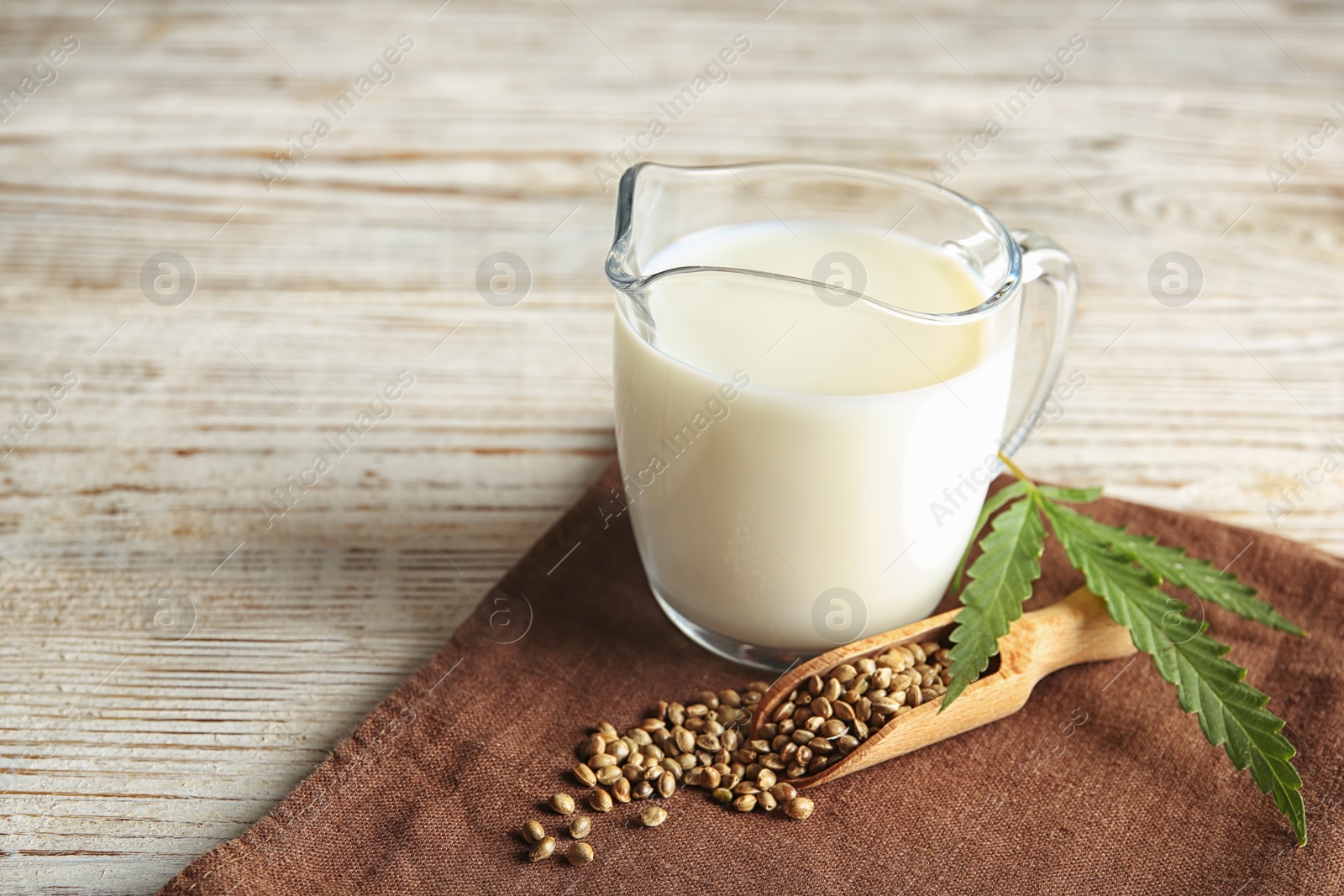 Photo of Scoop with hemp seeds and glass jug of milk on wooden table