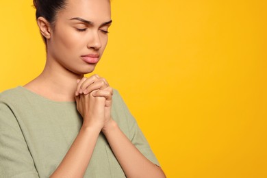 Photo of African American woman with clasped hands praying to God on orange background. Space for text