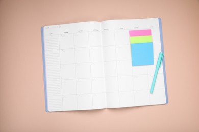 Open monthly planner, blank sticky notes and pen on beige background, top view. Space for text