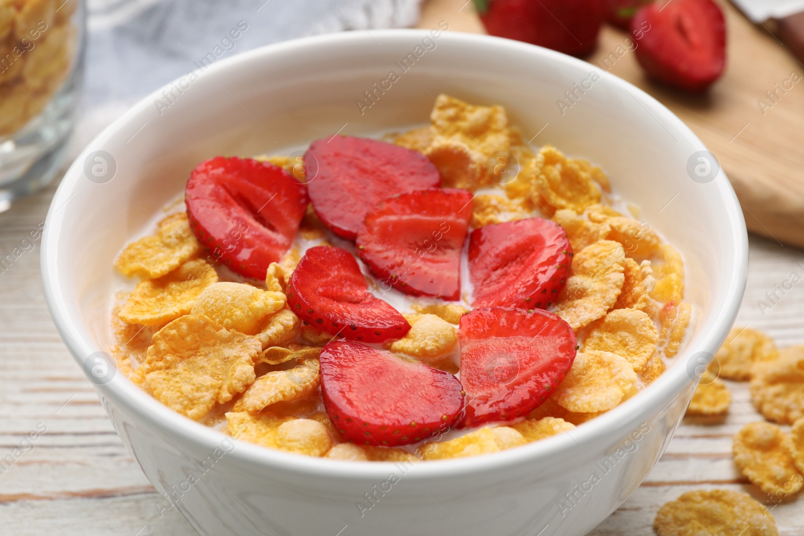 Photo of Bowl of tasty crispy corn flakes with milk and strawberries on white wooden table, closeup