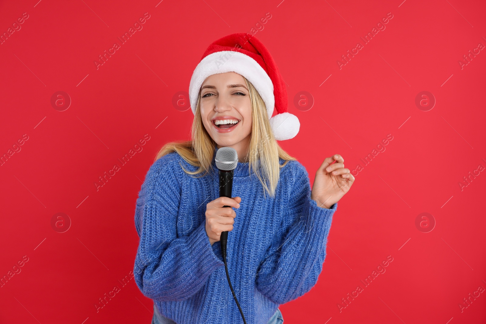 Photo of Happy woman in Santa Claus hat singing with microphone on red background. Christmas music