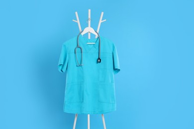 Turquoise medical uniform and stethoscope hanging on rack against light blue background