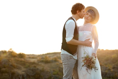 Happy newlyweds with beautiful field bouquet kissing outdoors