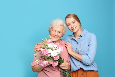 Photo of Young woman and her grandmother with flowers on light blue background
