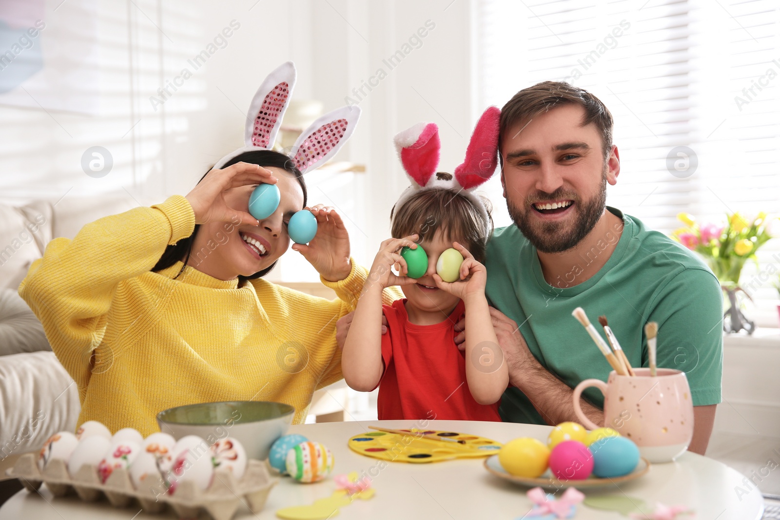 Photo of Happy family having fun while painting Easter eggs at table indoors