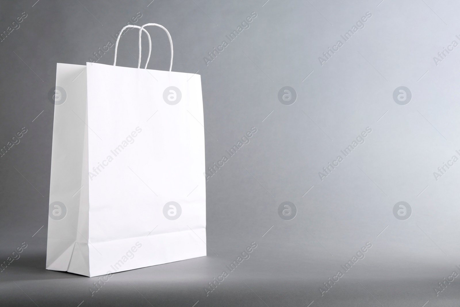 Photo of One white paper bag on grey background, space for text. Mockup for design