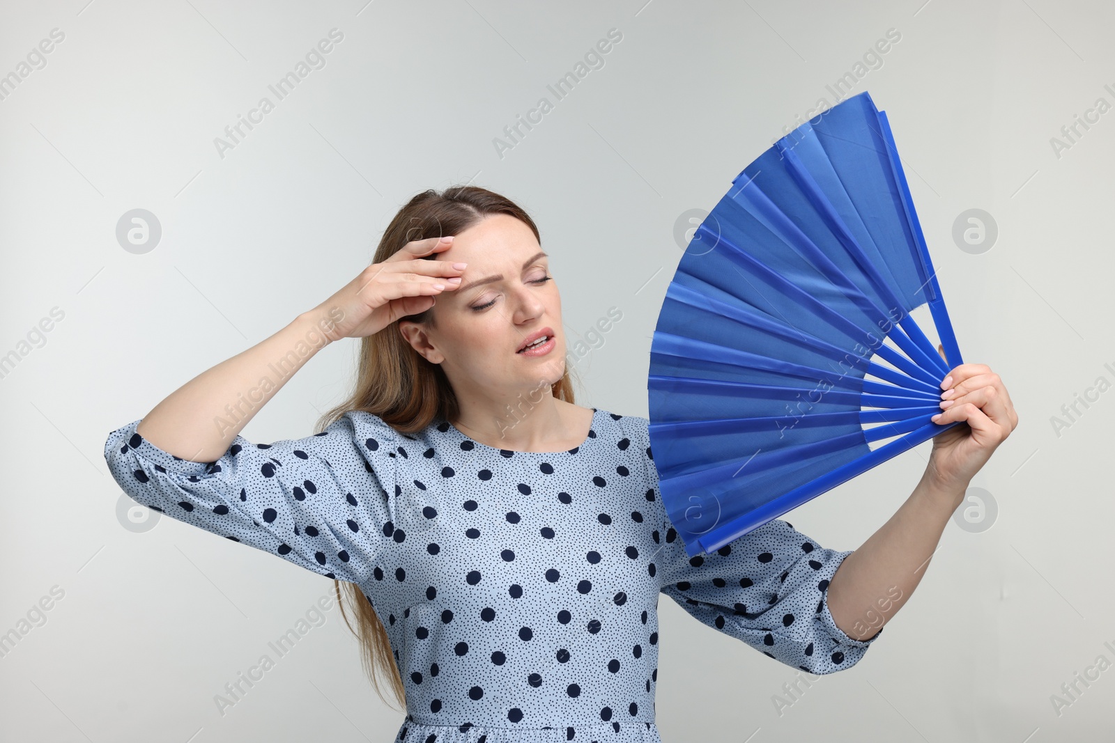 Photo of Beautiful woman waving blue hand fan to cool herself on light grey background