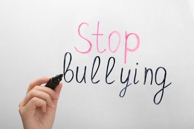 Photo of Woman writing phrase Stop Bullying on glass board against white background, closeup