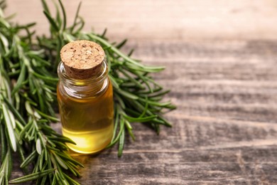 Photo of Bottle of essential oil and fresh rosemary on wooden table, closeup. Space for text