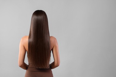 Photo of Hair styling. Woman with straight long hair on grey background, back view and space for text