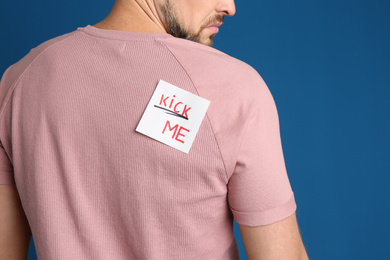 Photo of Man with KICK ME sticker on back against blue background, closeup. April fool's day