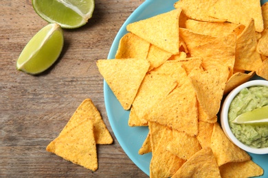 Photo of Plate with delicious mexican nachos chips, guacamole sauce and lime on wooden table, flat lay