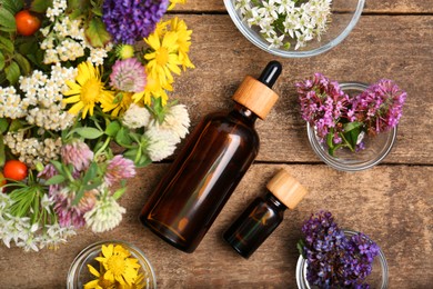 Photo of Bottles of essential oils surrounded by beautiful flowers on wooden table, flat lay