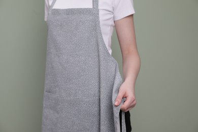 Photo of Woman putting on grey apron against light green background, closeup