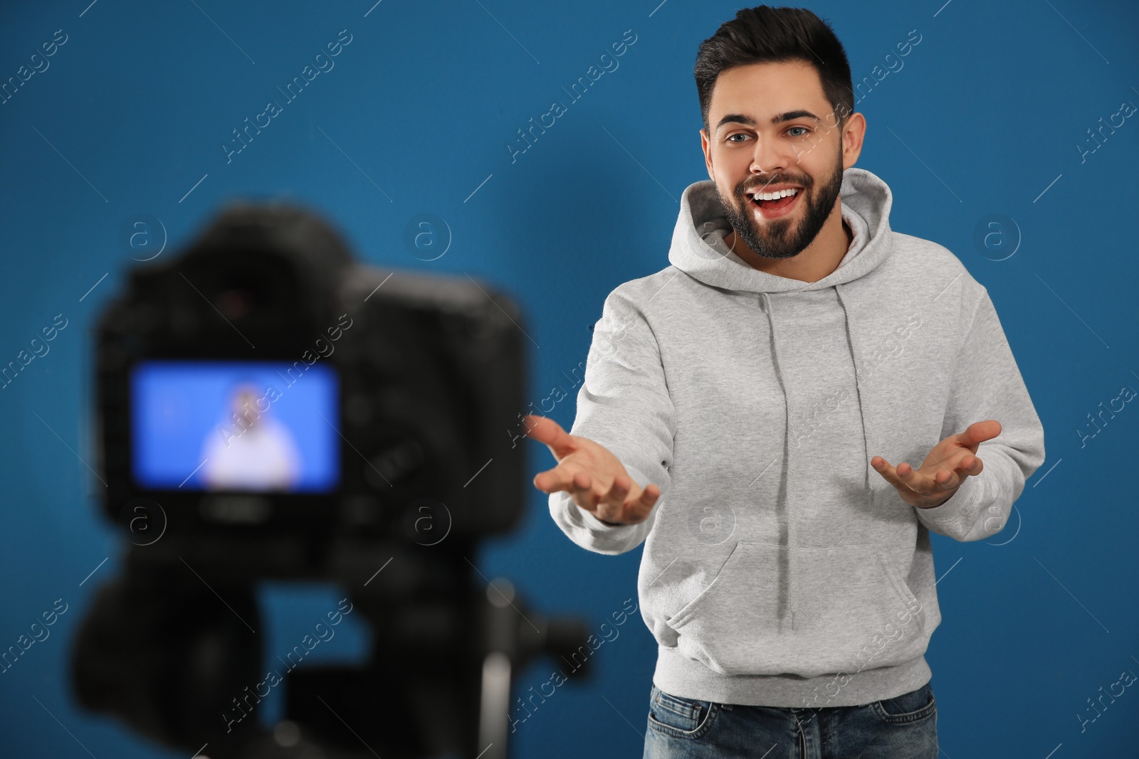 Photo of Young blogger recording video on camera against blue background