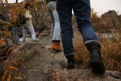 Photo of Group of friends crossing mountain river, focus on hiking boots