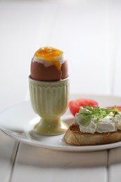 Fresh soft boiled egg in cup and sandwich on white wooden table