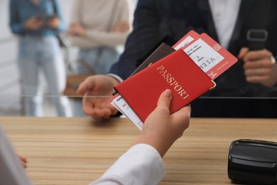 Agent giving passports with tickets to client at check-in desk in airport, closeup